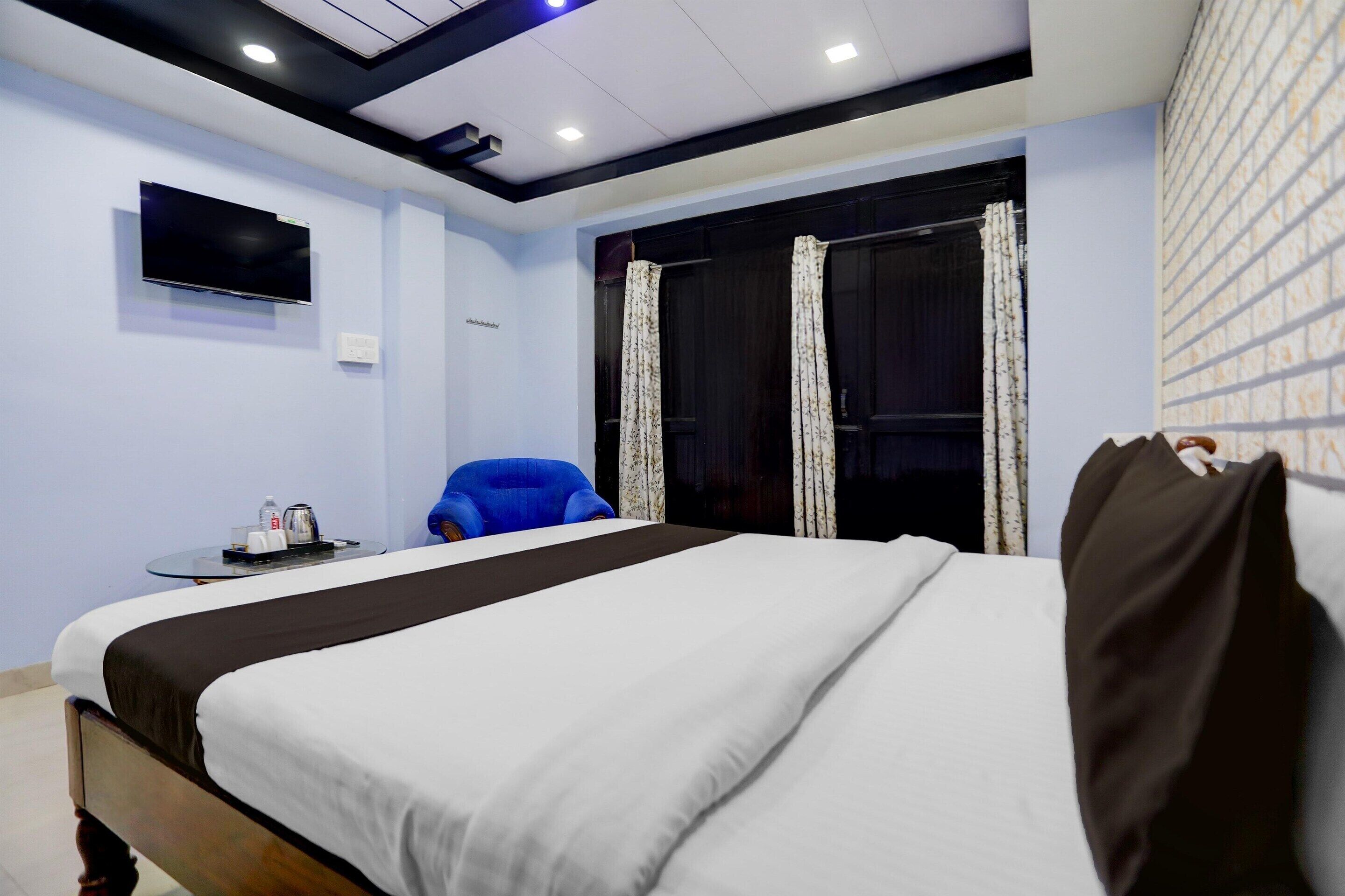 Une chambre d’hôtel avec un lit, un téléviseur fixé au mur, une petite table avec une chaise et une fenêtre avec des rideaux.