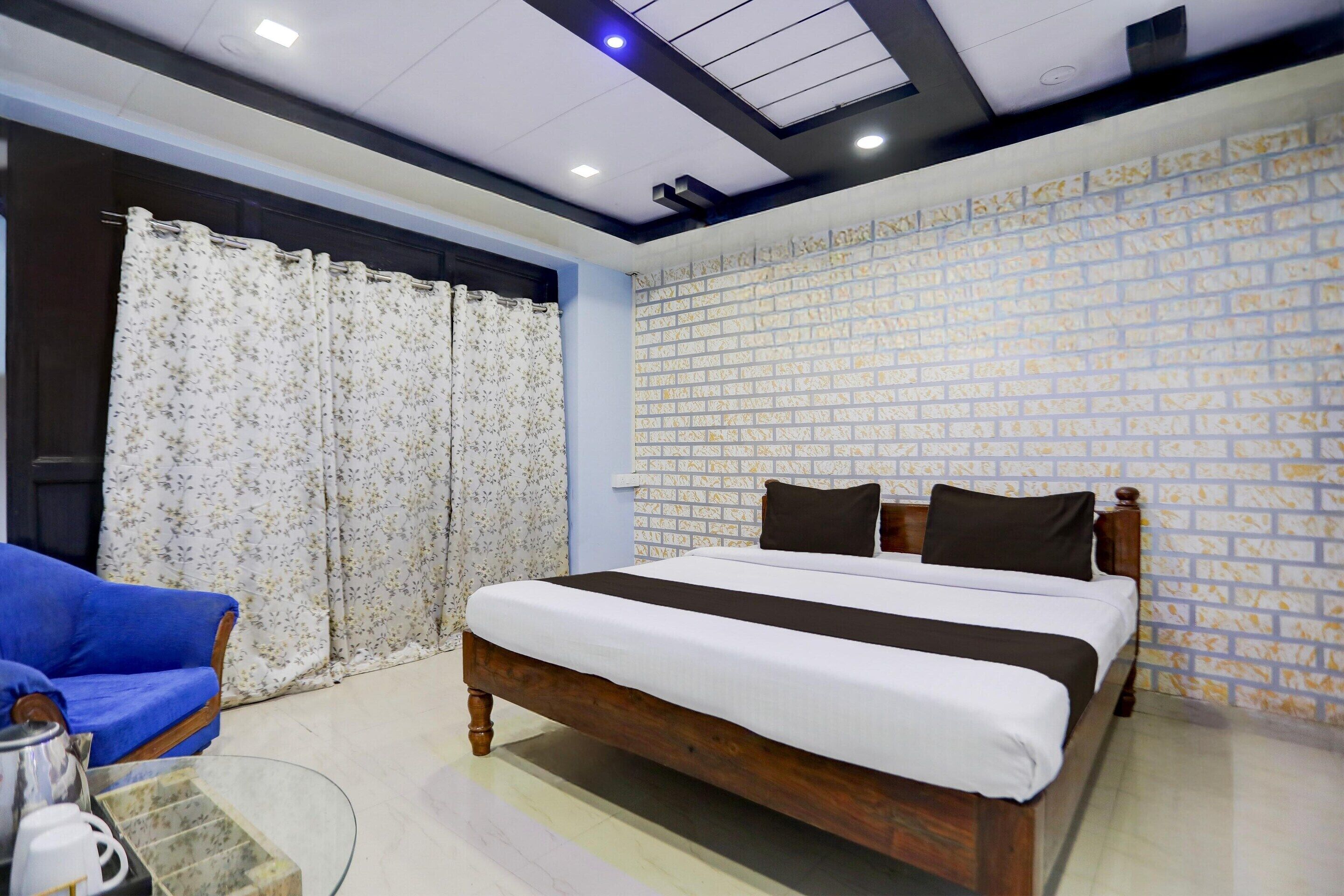 Un dormitorio con una cama de madera, un sofá azul, una mesita de centro de vidrio y una pared de ladrillo con diseño.