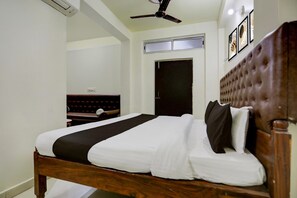 A bedroom with a wooden bed, a ceiling fan, a door, and framed artwork on the wall. - Deluxe Hotel Home Town (Patna)