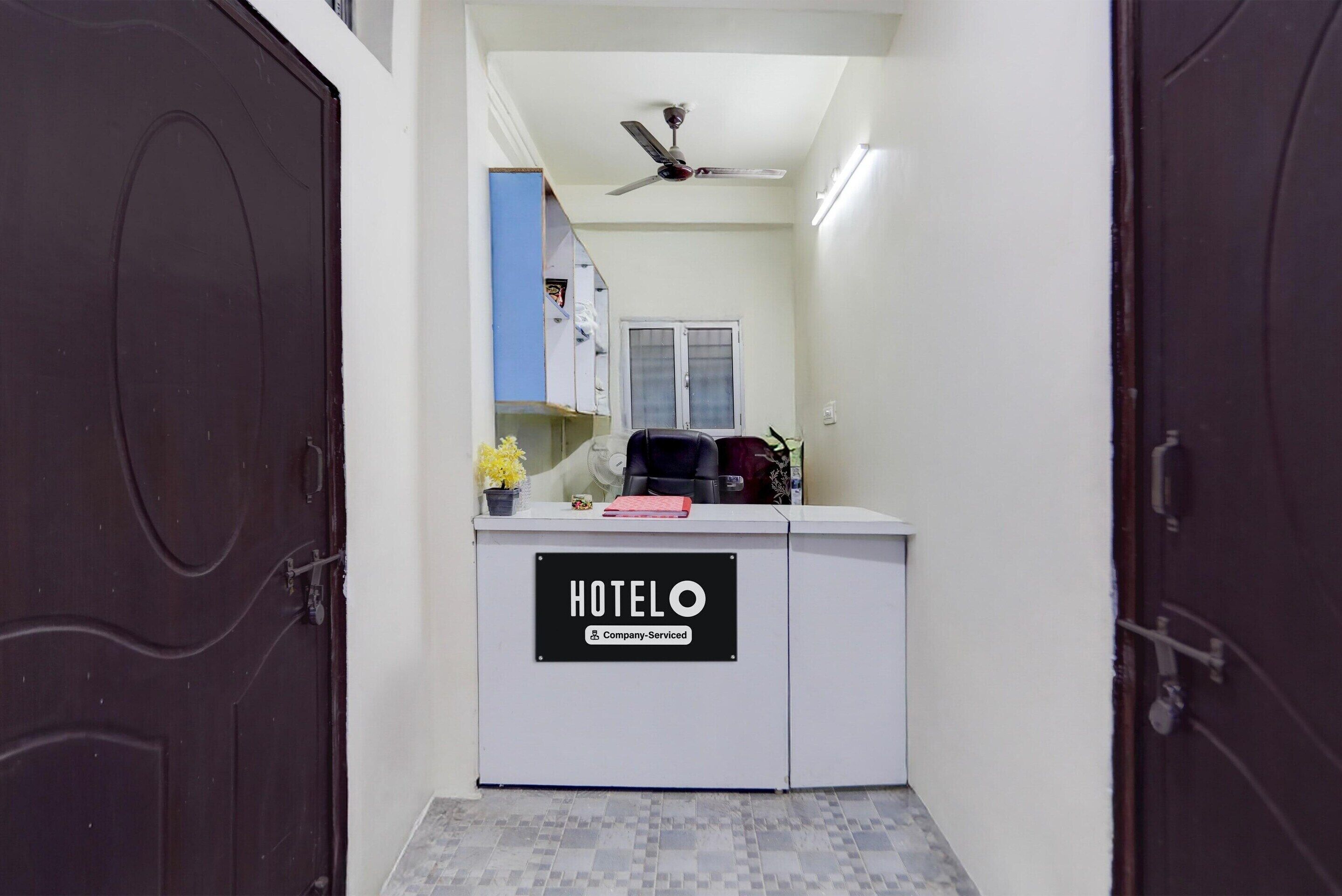 Una zona reception di un hotel con un cartello 'HOTELO', una ventola a soffitto, una finestra e un bancone con una pianta in vaso.
