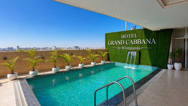 A rooftop pool with a view of the city, a sign for Hotel Grand Cabbana by Whitepanda, and potted plants along the pool's edge. - Grand Cabbana by White Panda Hotels (Amritsar)