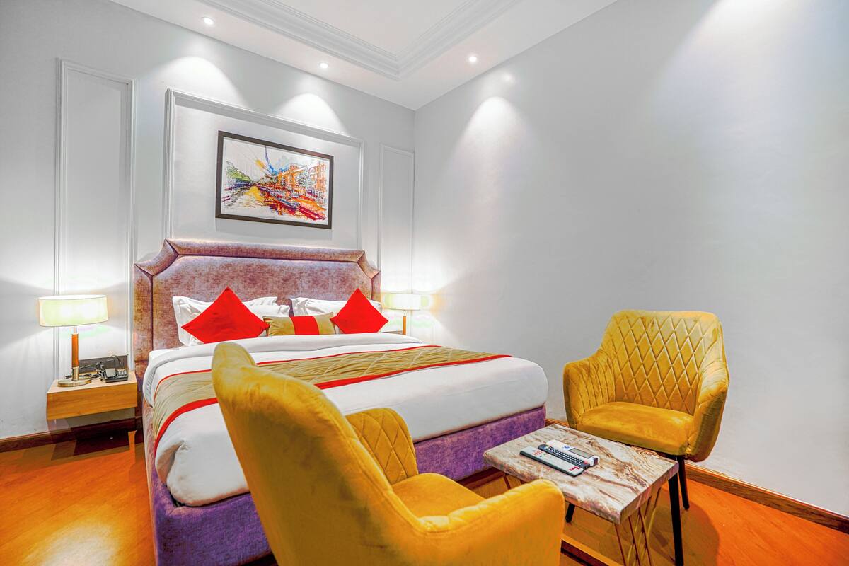 A hotel room with a bed, two chairs, a table, a lamp, and a painting on the wall.