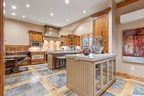 A spacious kitchen with wooden cabinets, a central island, and a dining area with a bench. - Luxury lodge with hot tub, sauna, game room, movie room & Deer Valley views (Park City)