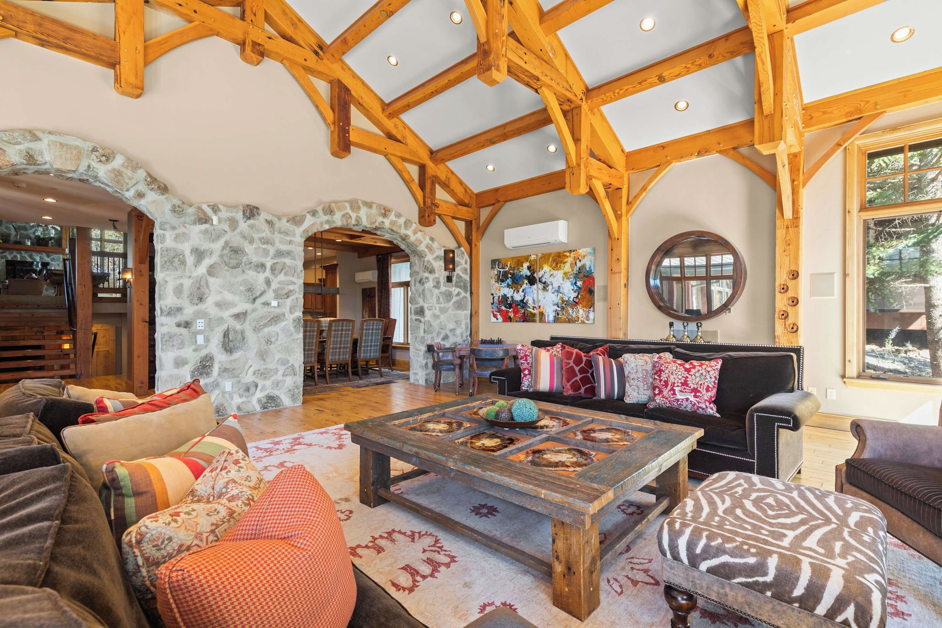 A spacious living area with a stone archway, wooden beams, a large painting, and a cozy seating arrangement.