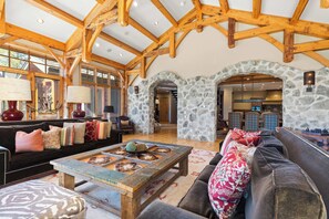A spacious living area with a high wooden ceiling, stone walls, and a fireplace. - Luxury lodge with hot tub, sauna, game room, movie room & Deer Valley views (Park City)