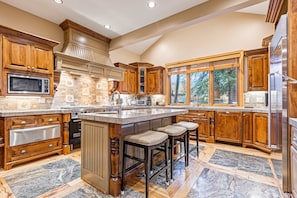 A spacious kitchen with wooden cabinets, a large island with bar stools, a built-in microwave, and a stainless steel refrigerator. - Luxury lodge with hot tub, sauna, game room, movie room & Deer Valley views (Park City)