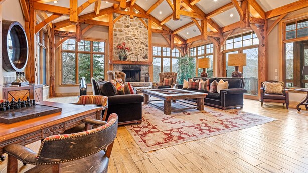 A spacious living room with a fireplace, wooden beams, and large windows. - Luxury lodge with hot tub, sauna, game room, movie room & Deer Valley views (Park City)