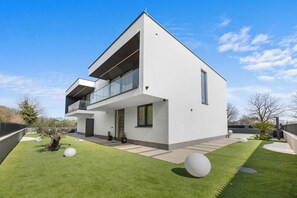 Une maison moderne à deux étages, dotée d’un toit plat, de grandes fenêtres et d’une pelouse bien entretenue.