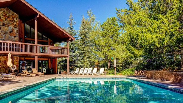 Une piscine avec des chaises longues, un mur en pierre et un bâtiment en bois doté d’un balcon.