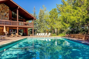 A pool with lounge chairs, a stone wall, and a wooden building with a balcony. - Charming year-round getaway - located close to downtown, shopping and dining (Park City)