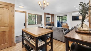 Un salon moderne avec une table à manger en bois, un canapé, un lustre et un téléviseur.