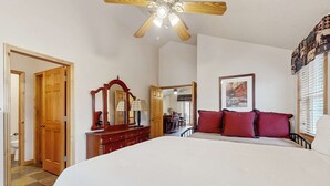 Un dormitorio con cama, cómoda, espejo, ventilador de techo y ventana con persianas.