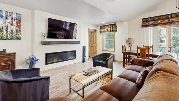 Una sala de estar con chimenea, televisor, comedor y un ventanal grande.