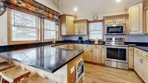 Una cocina con gabinetes de madera, horno de acero inoxidable, microondas y una isla grande con taburetes.