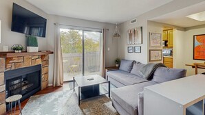 En stue med pejs, et fladskærms-tv, sofa, sofabord og en balkon med udsigt.