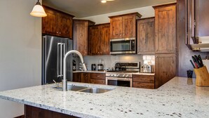 Una cocina con armarios de madera, electrodomésticos de acero inoxidable, encimera de granito e iluminación colgante.