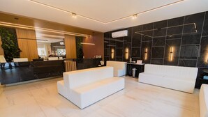 A modern lobby with a reception desk, white sofas, and a black marble wall. - Vila do Centro (Bombinhas)
