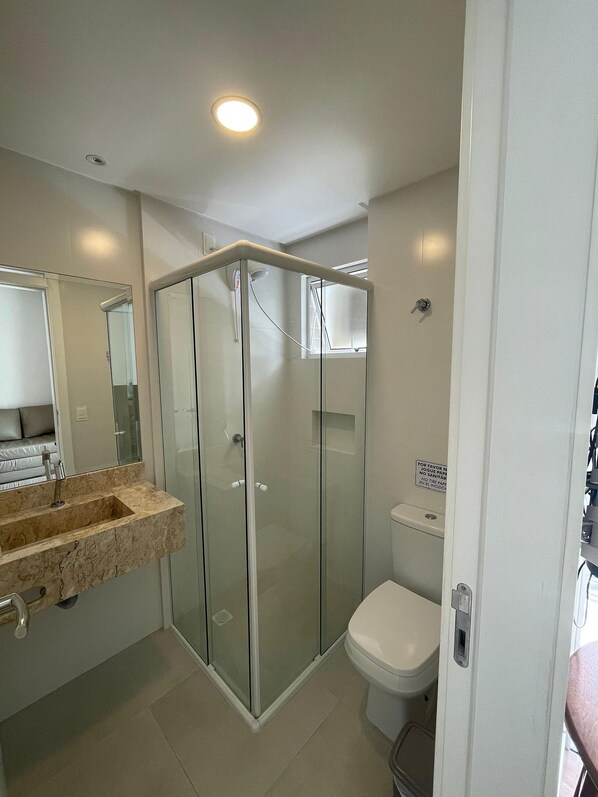 Et moderne badeværelse med en brusekabine i glas, en marmorvask og et toilet.