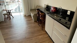 A compact kitchen with a dining area, a sofa, and a view of the outside. - Vila do Centro (Bombinhas)