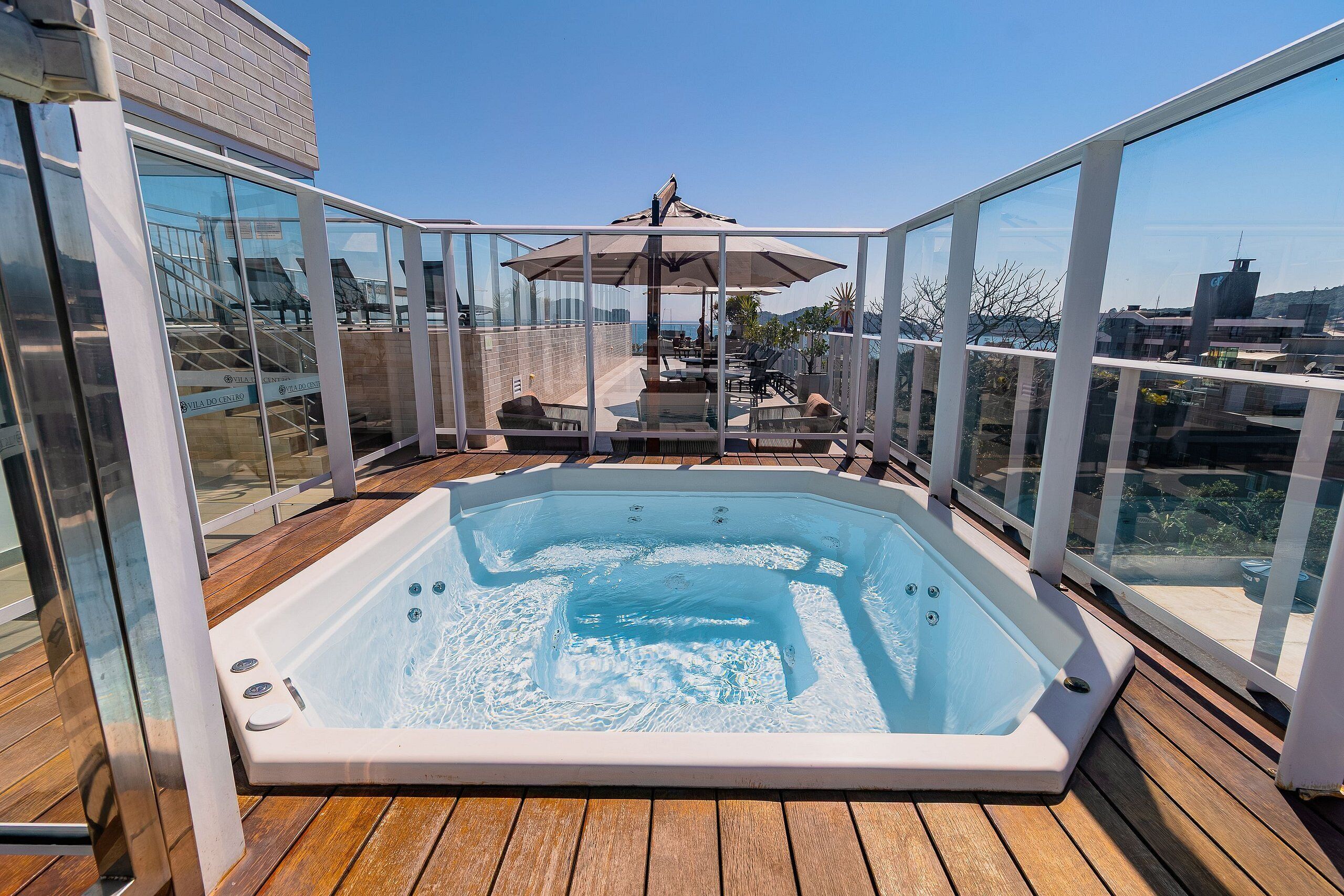A hot tub on a wooden deck with glass walls, a patio area, and a view of the city.