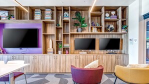 A modern office space with a large flat-screen TV, two smaller monitors, wooden shelving with books and decorative items, and comfortable seating. - Walk-to-lift studio with hot tub, sauna, pool, gym, & game room - Dog friendly (Park City)