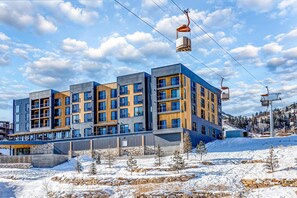 A modern multi-story building with a ski lift, surrounded by snow and trees. - Walk-to-lift studio with hot tub, sauna, pool, gym, & game room - Dog friendly (Park City)