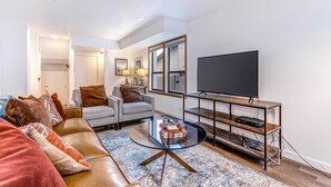 Ett modernt vardagsrum med en soffa i läder, ett soffbord i glas, en tv på ett träställ och en mönstrad matta.