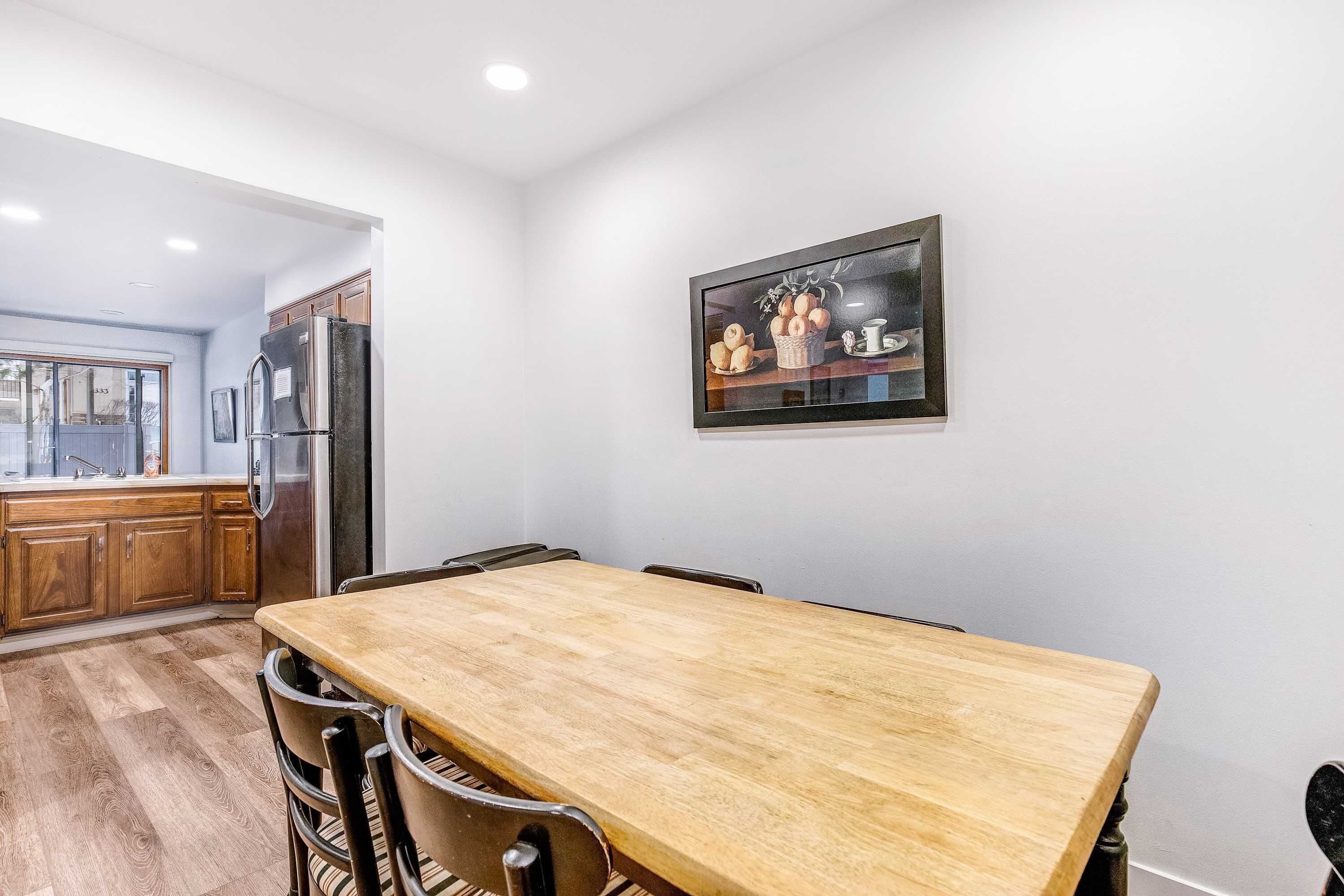 Un comedor con una mesa y sillas de madera, un refrigerador y una cocina con armarios de madera.