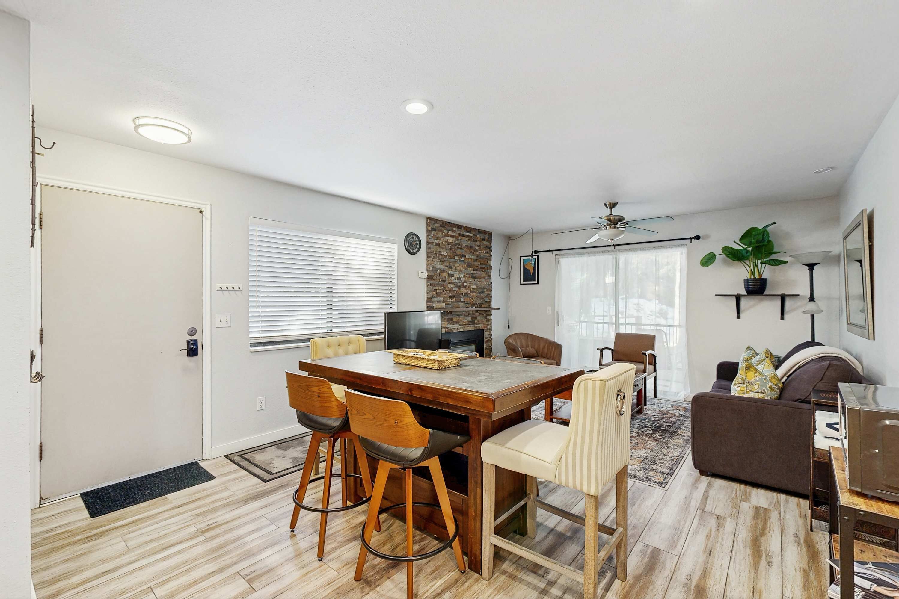 A dining area with a wooden table and chairs, a sofa, a television, and a ceiling fan.
