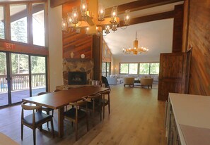 A spacious room with a wooden dining table, chairs, a stone fireplace, and large windows offering views of the outdoors. - Cozy condo with  fireplace, clubhouse access, free Wifi & shared Pool & Hot Tub (Park City)