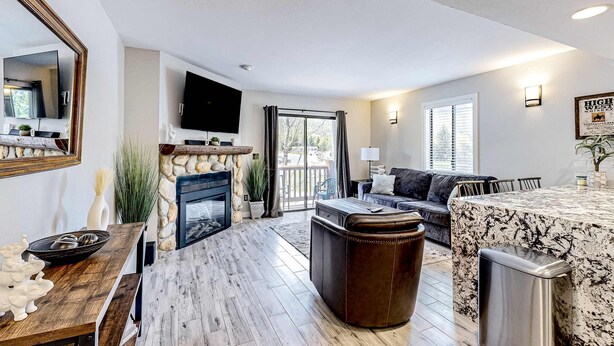 A modern living room with a fireplace, a stone wall, a wooden floor, a sofa, a coffee table, and a kitchen area with a marble countertop. - Updated condo w/ ski & mountain views, walk to slopes, free Wifi (Park City)