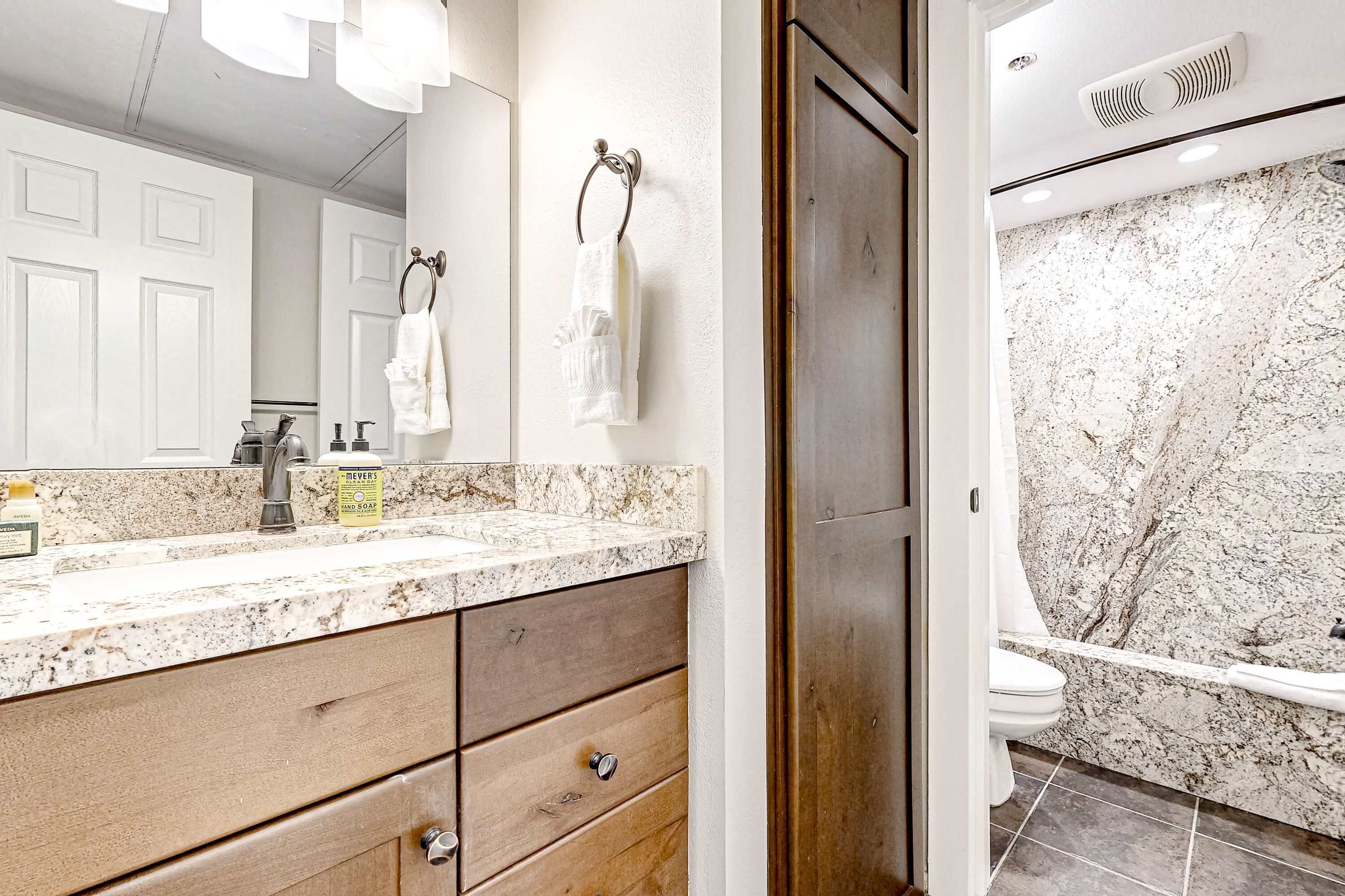 Une salle de bain avec un lavabo en marbre, un meuble-lavabo en bois et une douche dont le mur est également en marbre.