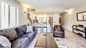 A modern living room with a sofa, coffee table, and leather chair. A kitchen with white cabinets and stainless steel appliances is visible in the background. - Updated condo w/ ski & mountain views, walk to slopes, free Wifi (Park City)
