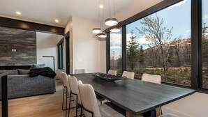 Un comedor moderno con una mesa de madera oscura, seis sillas y un ventanal que ofrece vistas a árboles y colinas.