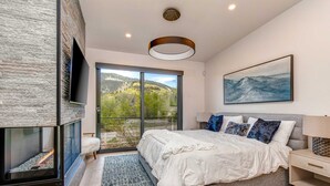 Un dormitorio moderno con chimenea, una cama grande, vistas al exterior y un cuadro en la pared.