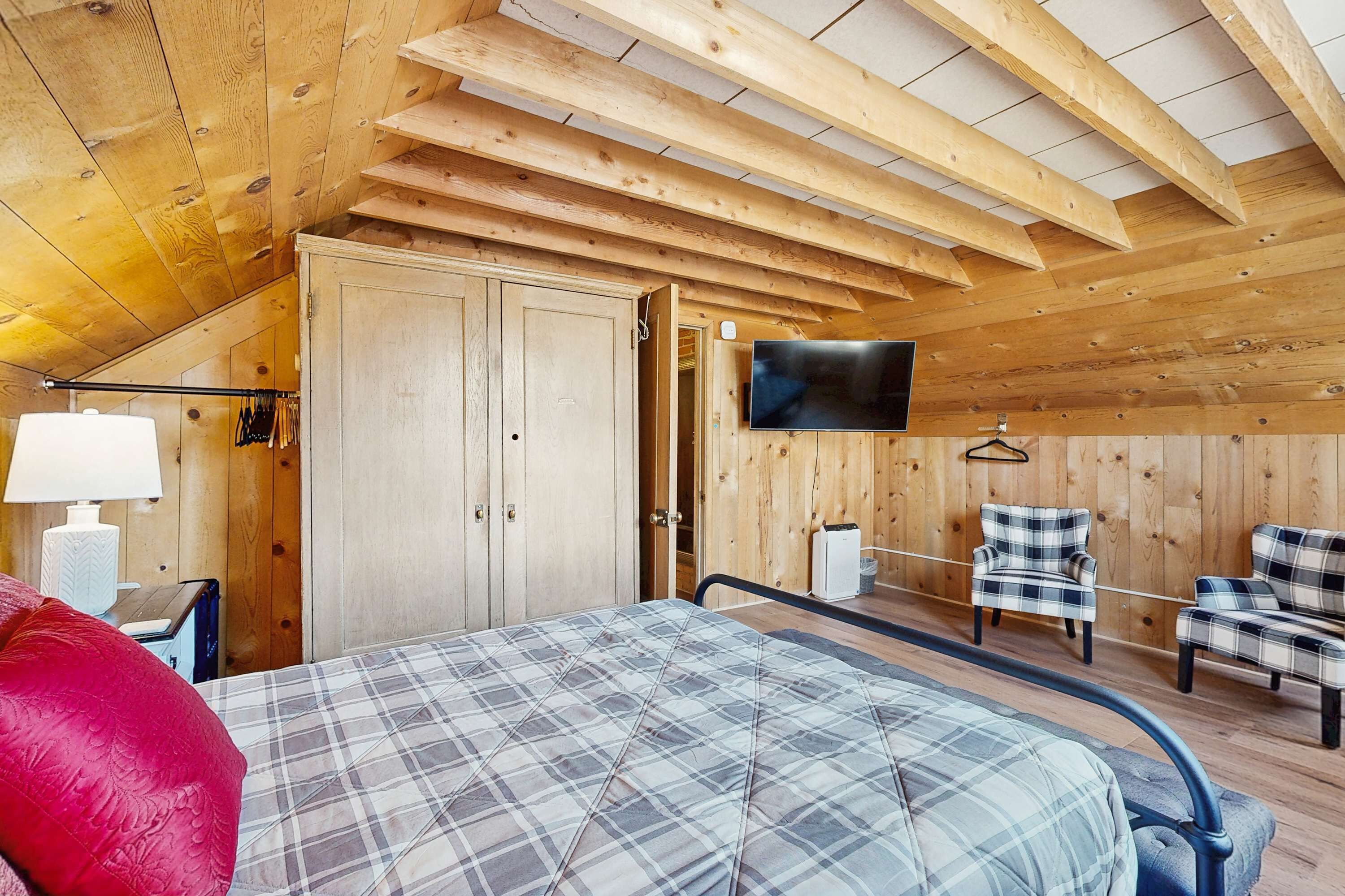 Un interior de madera con una cama, un televisor y dos sillas.