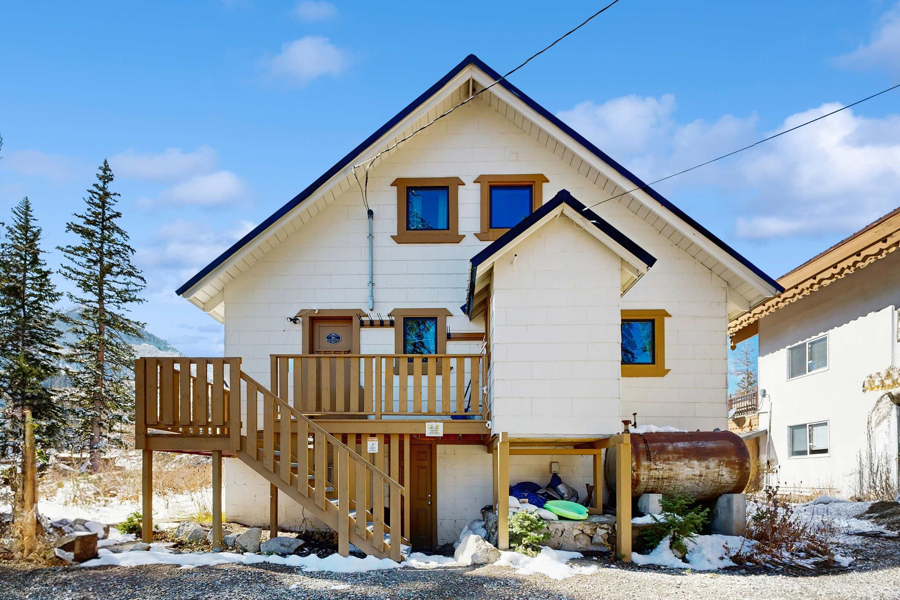 Une maison à deux étages avec un escalier en bois, un balcon et un garage contenant un grand objet cylindrique.