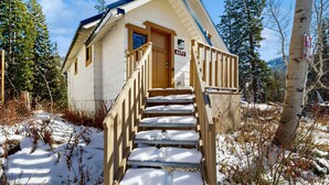 Eine Holzhütte mit einer Holztreppe, die zu einer Tür mit der Aufschrift '8171' führt, umgeben von Schnee und Bäumen.