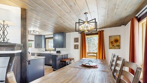 Ein Essbereich mit Holztisch und -stühlen, im Hintergrund eine Küche und eine Decke mit sichtbaren Balken.