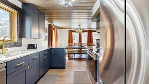 Eine moderne Küche mit dunklen Schränken, einem Edelstahlkühlschrank und einem Essbereich mit Holztisch.