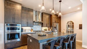 A modern kitchen with stainless steel appliances, wooden cabinets, and a central island with bar stools. - Brand-new townhome with views & hot tub  - 12 mins to Park City & Deer Valley (Hideout)