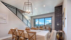 A dining area with a table set for six, a staircase, and a large window with a mountain view. - Brand-new townhome with views & hot tub  - 12 mins to Park City & Deer Valley (Hideout)