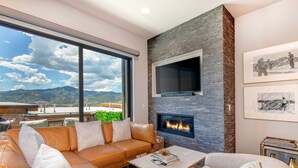 A modern living room with a leather sofa, a fireplace, a flat-screen TV, and a large window offering a mountain view. - Brand-new townhome with views & hot tub  - 12 mins to Park City & Deer Valley (Hideout)
