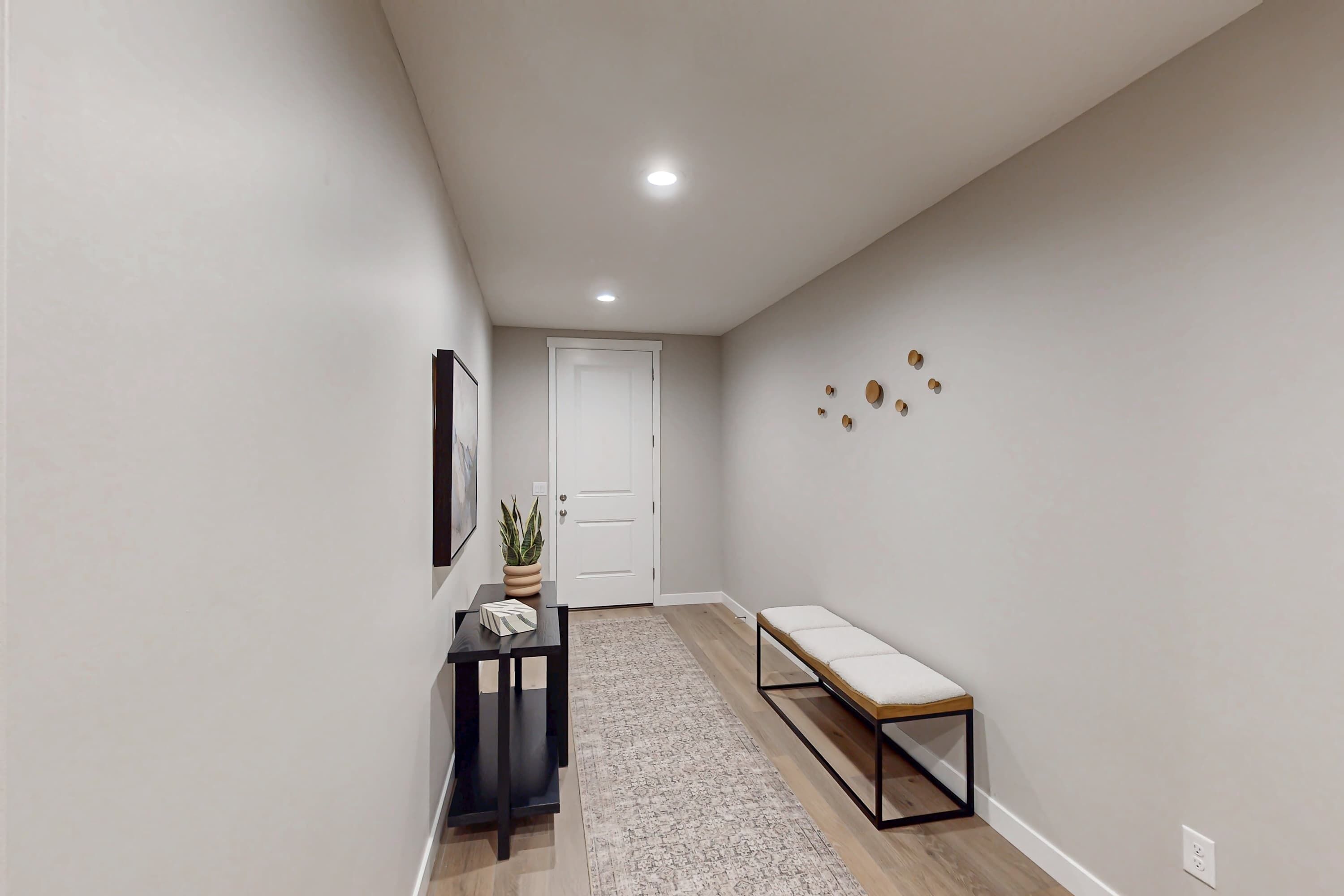 A hallway with a bench, a door, a small table with a plant, and wall decorations.