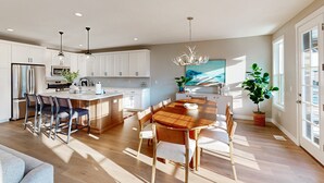 A modern kitchen with white cabinets, a wooden dining table, and bar stools. - Bright Spacious & Modern Condo with fireplace and gas grill (Heber City)
