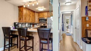 Una cocina con armarios de madera, microondas, refrigerador y una barra con taburetes.