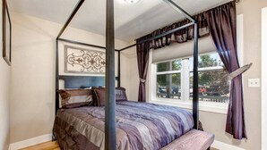 Una cama con dosel, un cabecero, un banco, una ventana con cortinas y un adorno en la pared.