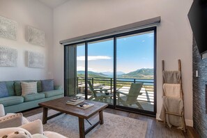 A modern living room with a sofa, coffee table, and chairs, a balcony with a view of mountains, and a fireplace. - Brand-new townhome with views, shuffleboard - 12 mins to Park City & Deer Valley (Hideout)