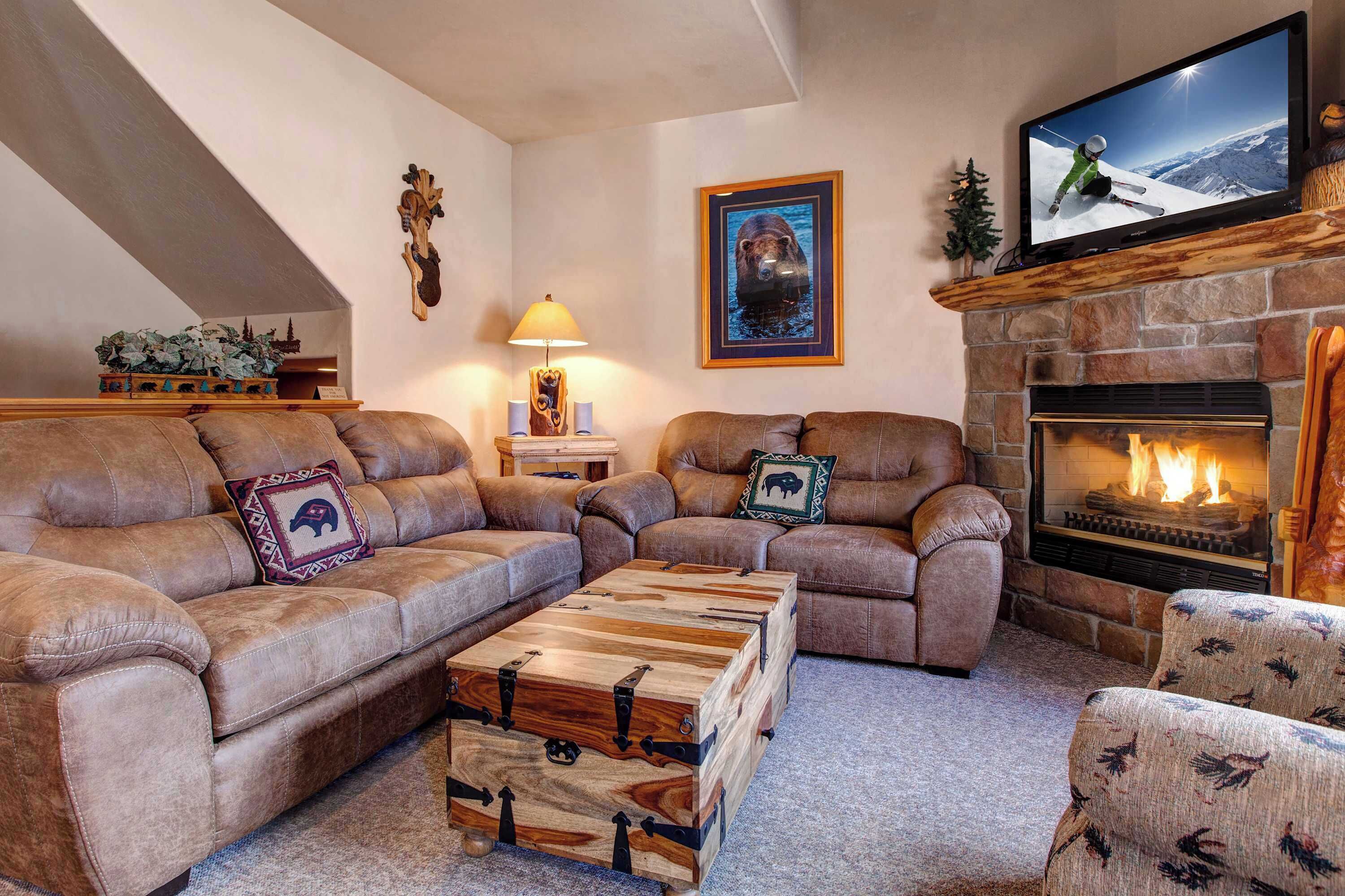 A cozy living room with leather sofas, a wooden coffee table, a fireplace, and a mounted TV.