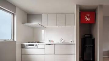 Une cuisine moderne avec des meubles blancs, un réfrigérateur noir et un panneau rouge accroché au mur.